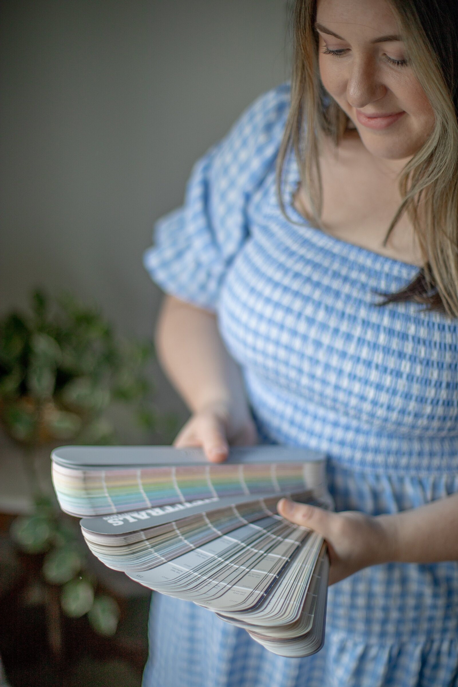 Kayla holding an open fan of paint and fabric swatches, with greenery behind her