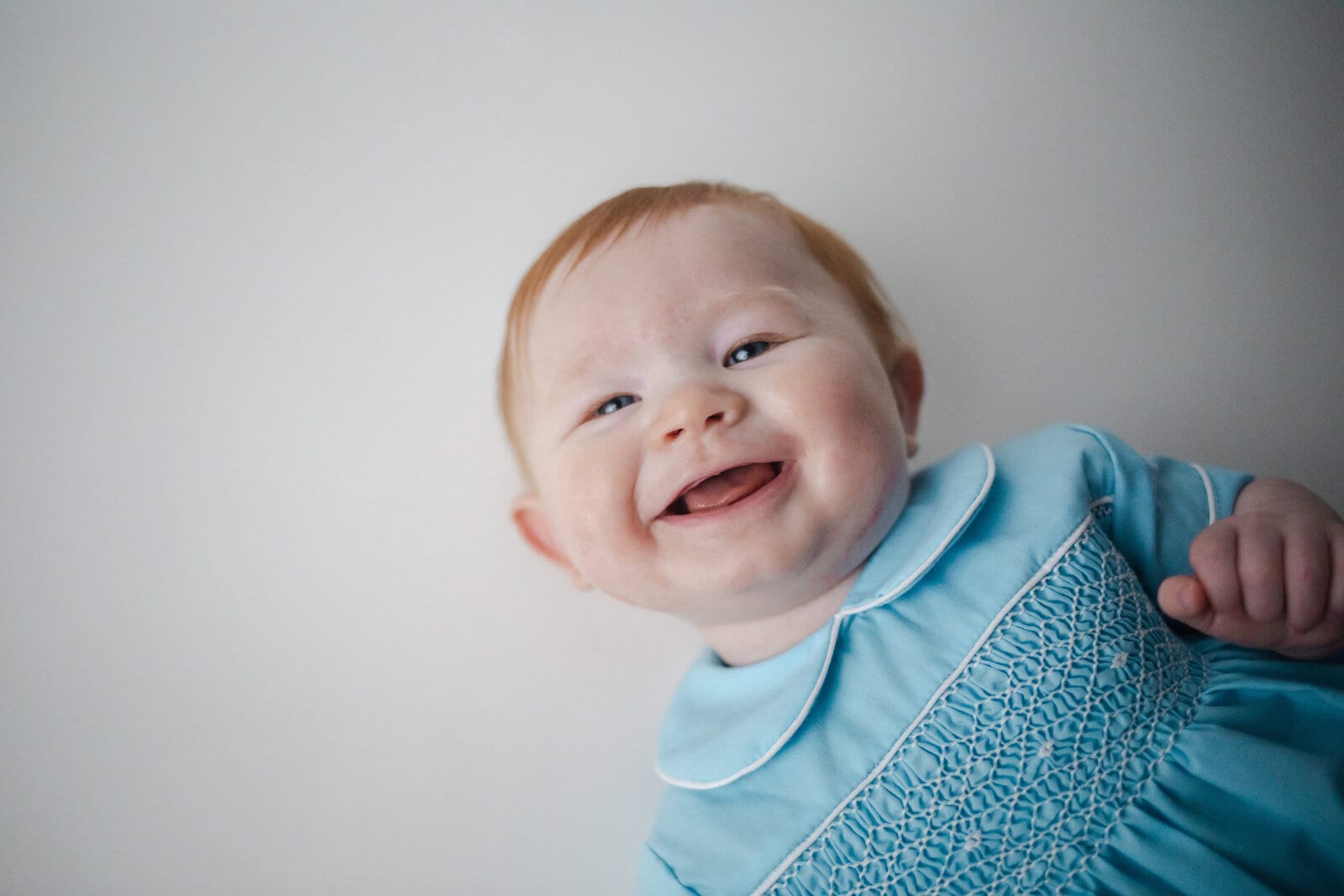 Kayla's baby son Brooks, laughing, in a pale blue smocked romper against a white background