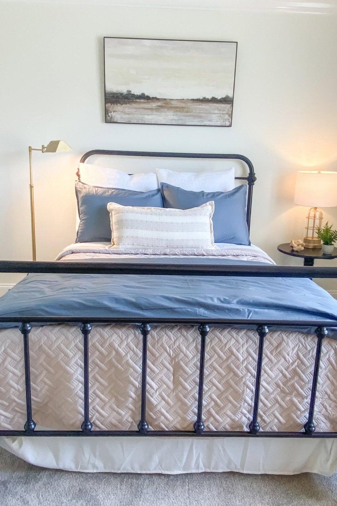 A bedroom with a black iron bedstead and a woven bench at its foot