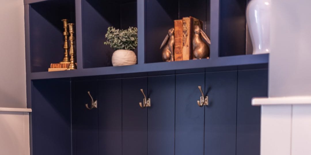 A navy mudroom with brass hooks, lockers and woven baskets