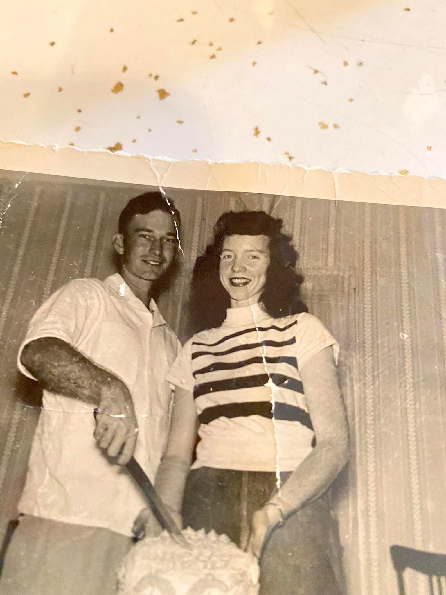 A creased sepia snapshot of Gloria Dean and her husband as a young couple, cutting a white cake together